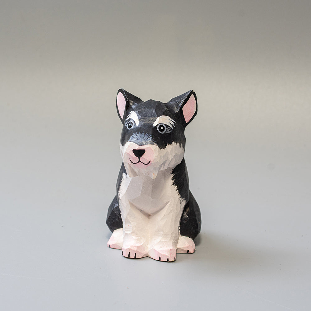 Hand carved wooden schnauzer figurine in seated pose with upright ears and textured black and white finish. 
