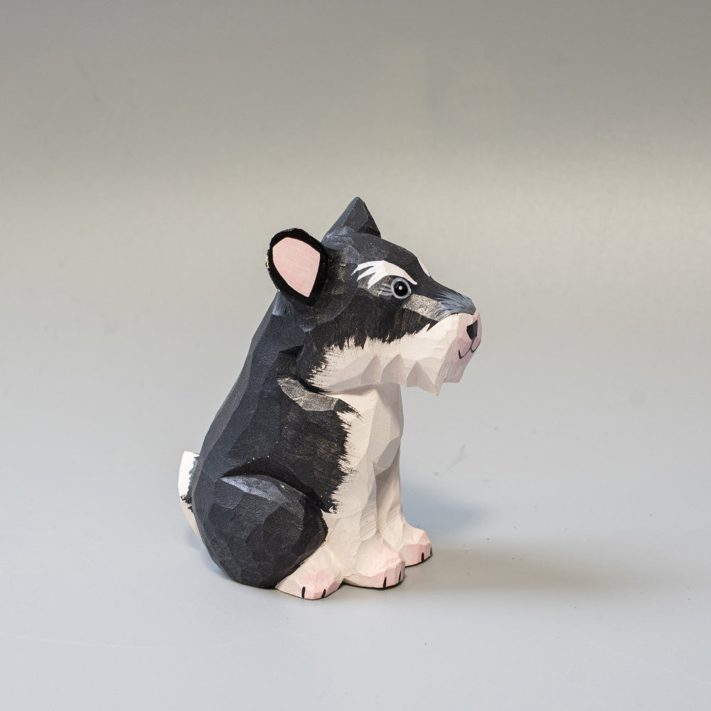 Hand carved wooden schnauzer figurine in seated pose with upright ears and textured black and white finish.