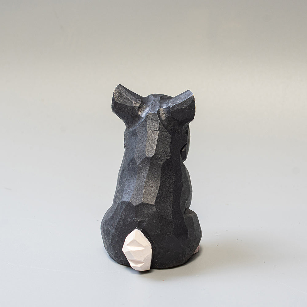 Hand carved wooden schnauzer figurine in seated pose with upright ears and textured black and white finish. 