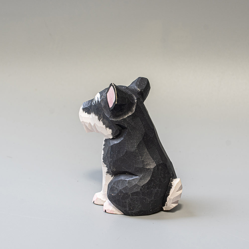 Hand carved wooden schnauzer figurine in seated pose with upright ears and textured black and white finish. 
