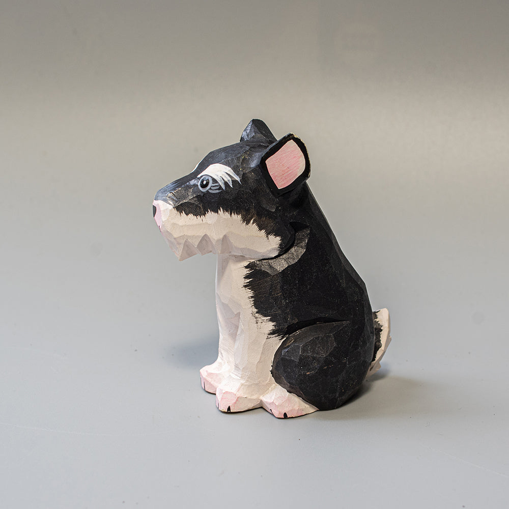 Hand carved wooden schnauzer figurine in seated pose with upright ears and textured black and white finish. 
