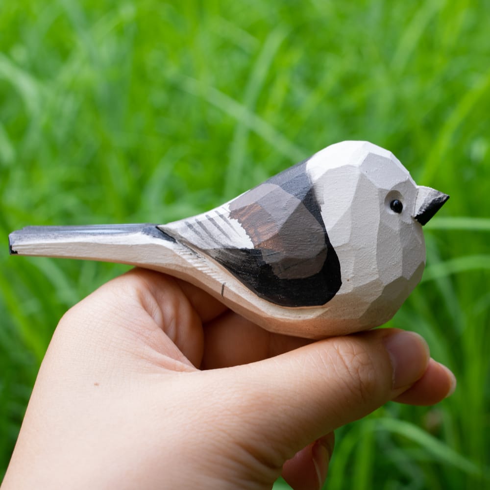 Wooden shima enaga figurine held in a hand with a green grass background