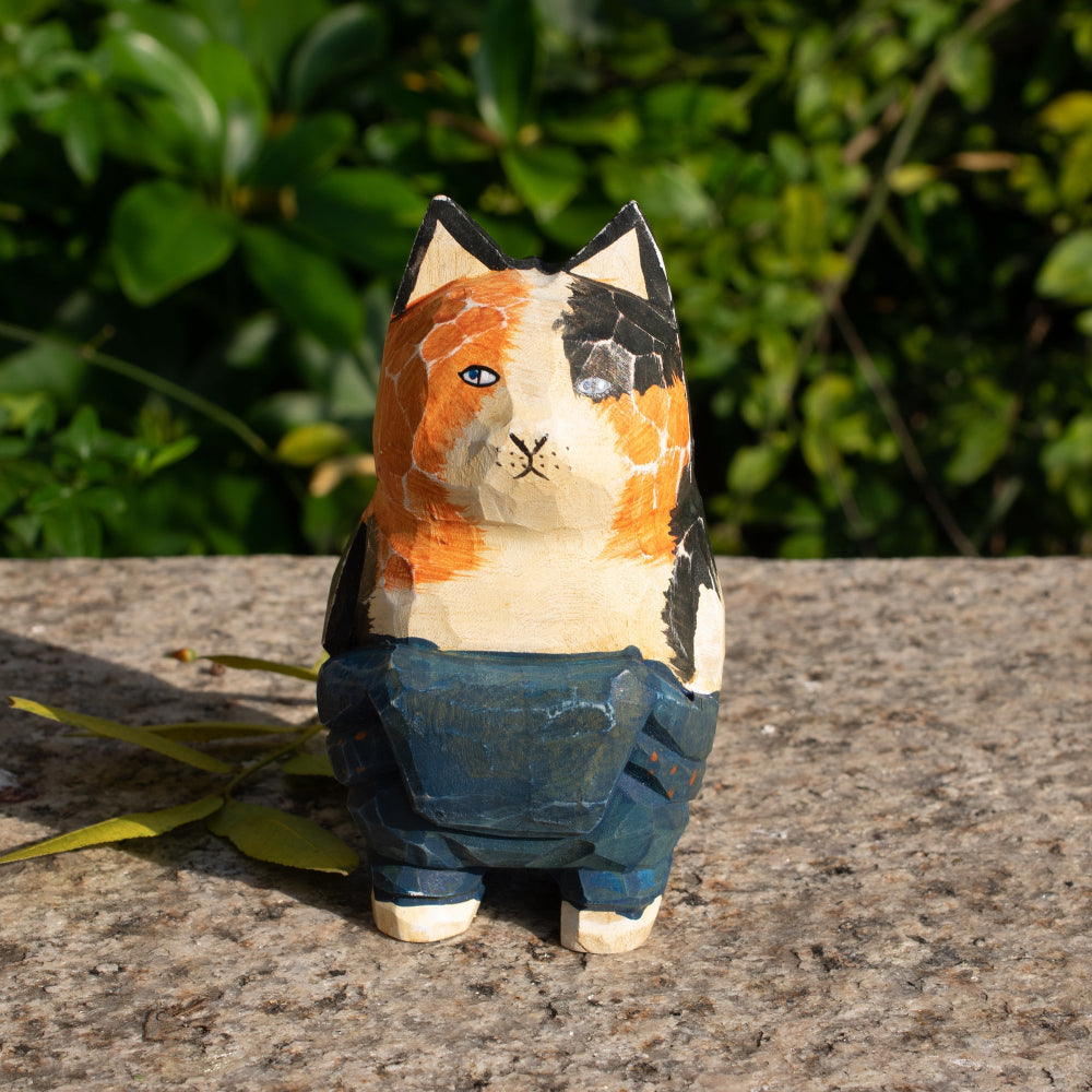 Hand-carved wooden figurine of a lounging calico cat in overalls, a playful addition to cat lover decor.