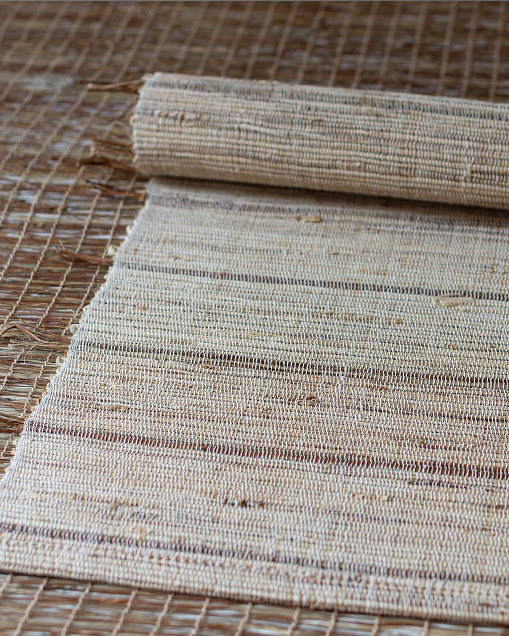 A hand-woven table runner made of natural ramie fiber, shown partially unrolled on a dark wood table to highlight its coarse, rustic texture.