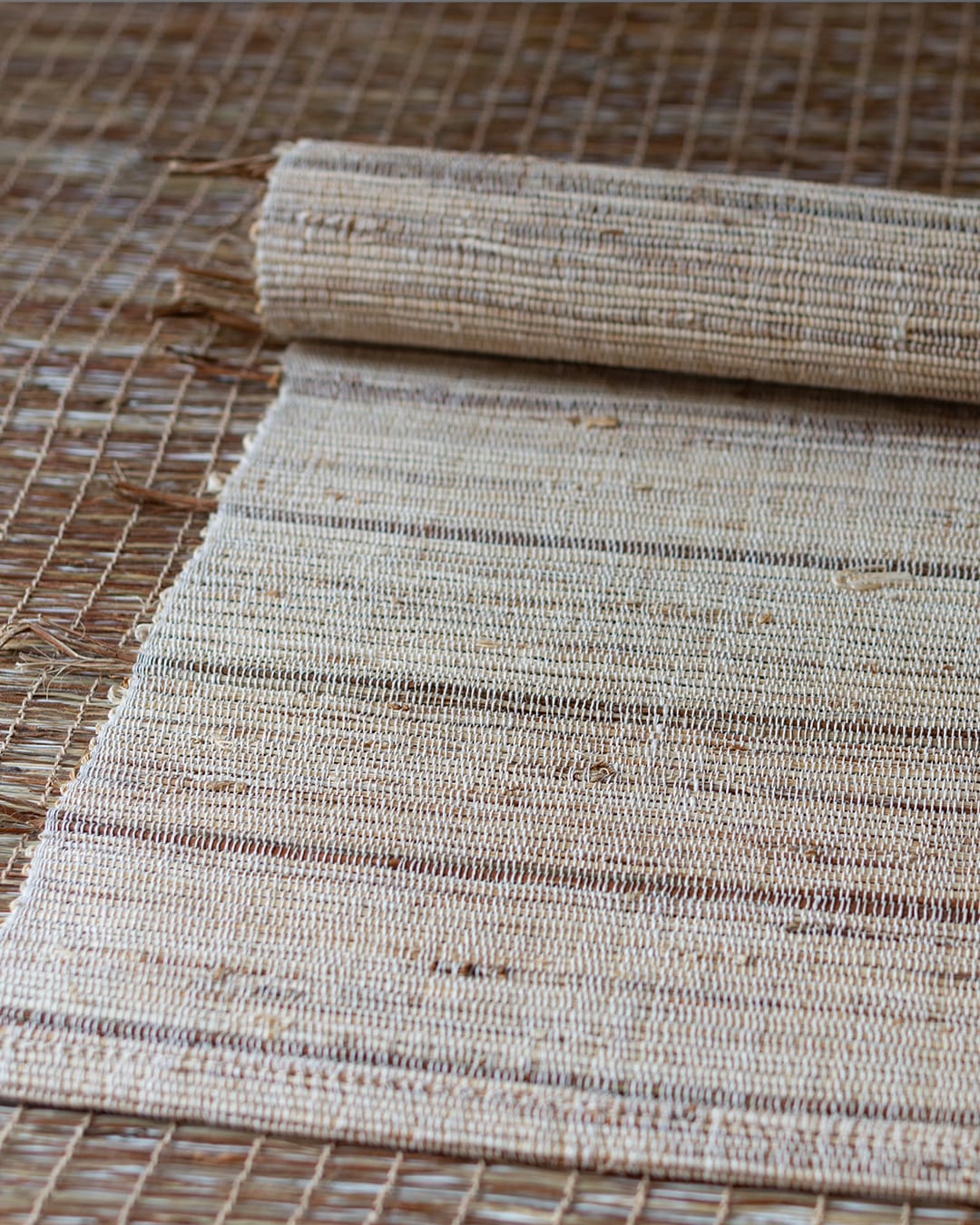 A hand-woven table runner made of natural ramie fiber, shown partially unrolled on a dark wood table to highlight its coarse, rustic texture.