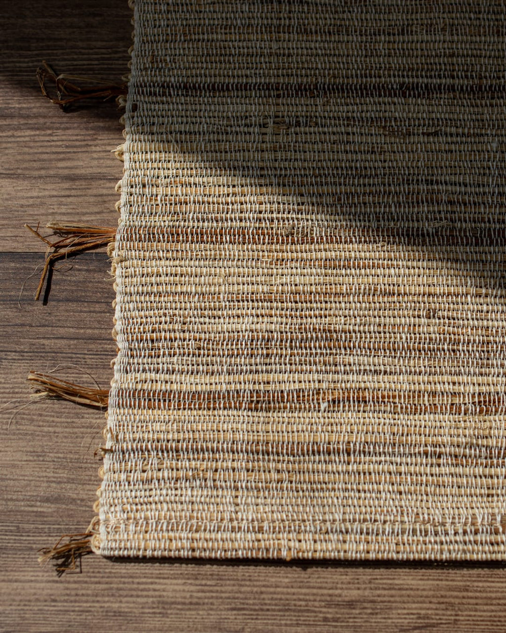 A hand-woven table runner made of natural ramie fiber, shown partially unrolled on a dark wood table to highlight its coarse, rustic texture.