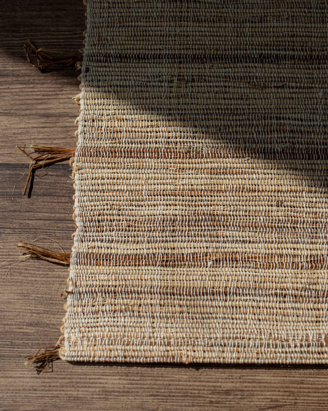 A hand-woven table runner made of natural ramie fiber, shown partially unrolled on a dark wood table to highlight its coarse, rustic texture.