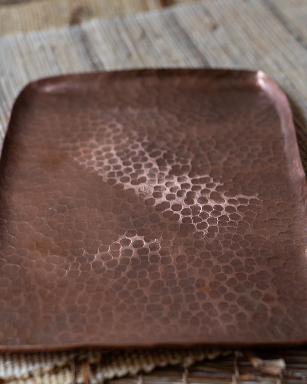 A rectangular, hand-hammered solid copper tray with a textured Tsuchime surface on a linen mat.