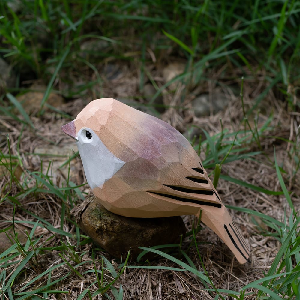 Wooden Vinous-throated Parrotbill figurine on grass and stones