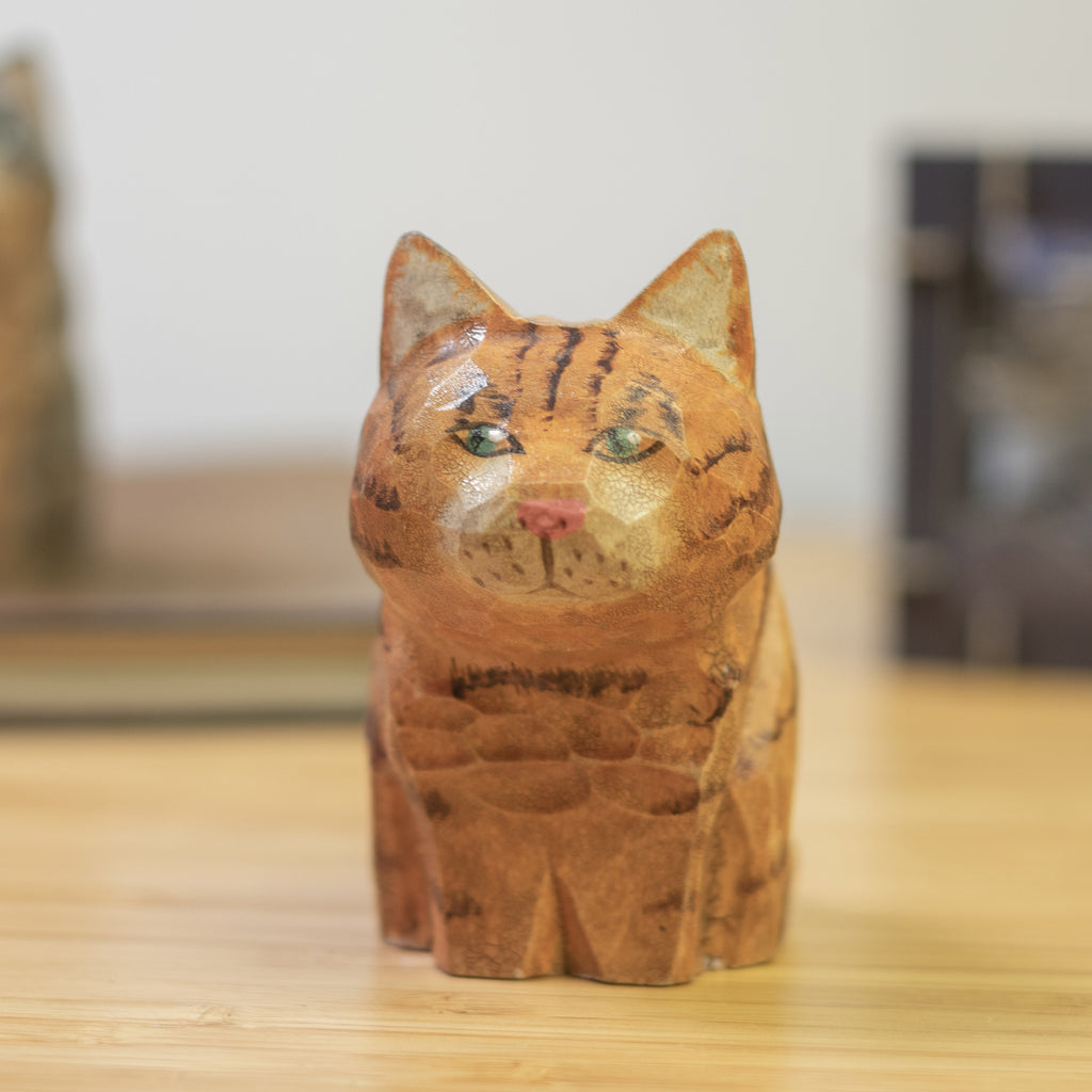 A hand-carved wooden figurine of an orange tabby cat with a vintage aesthetic finish.