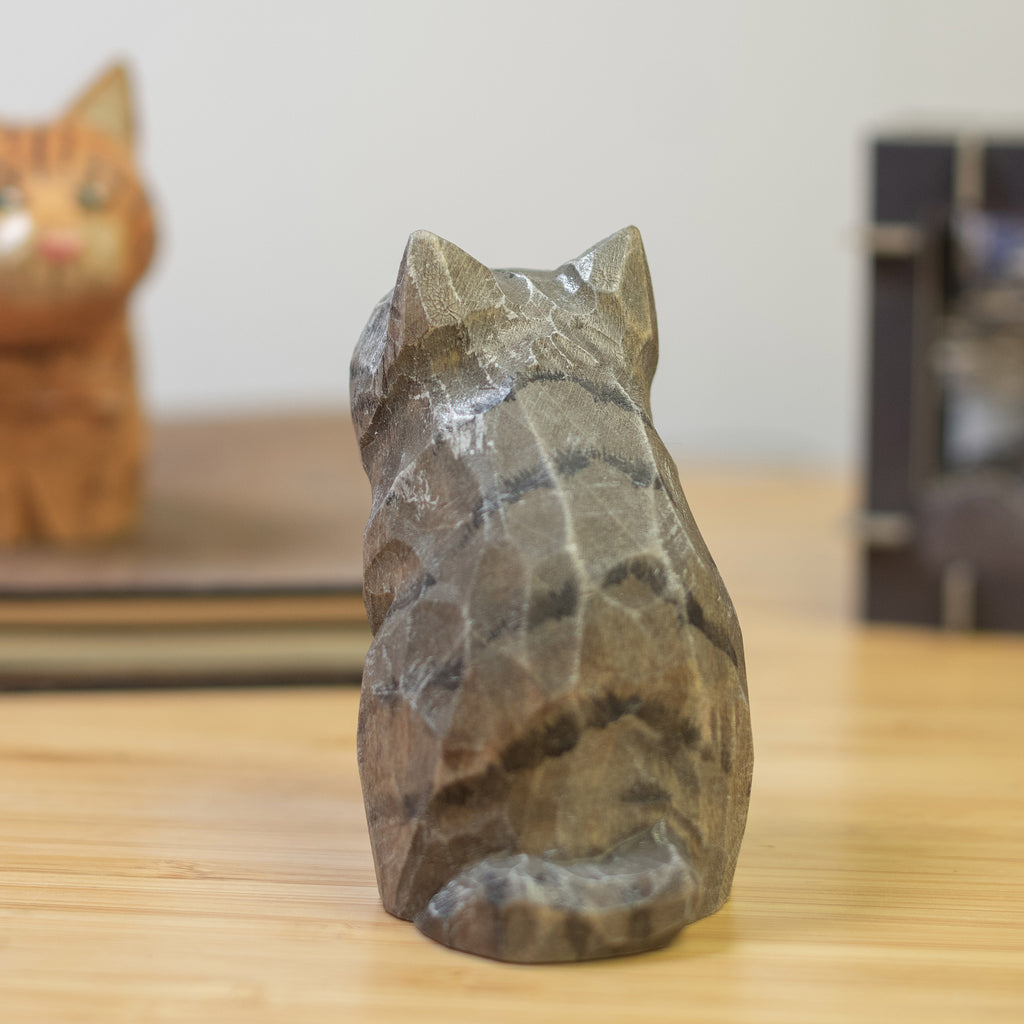 A hand-carved wooden figurine of a gray tabby cat, placed on a wooden surface.