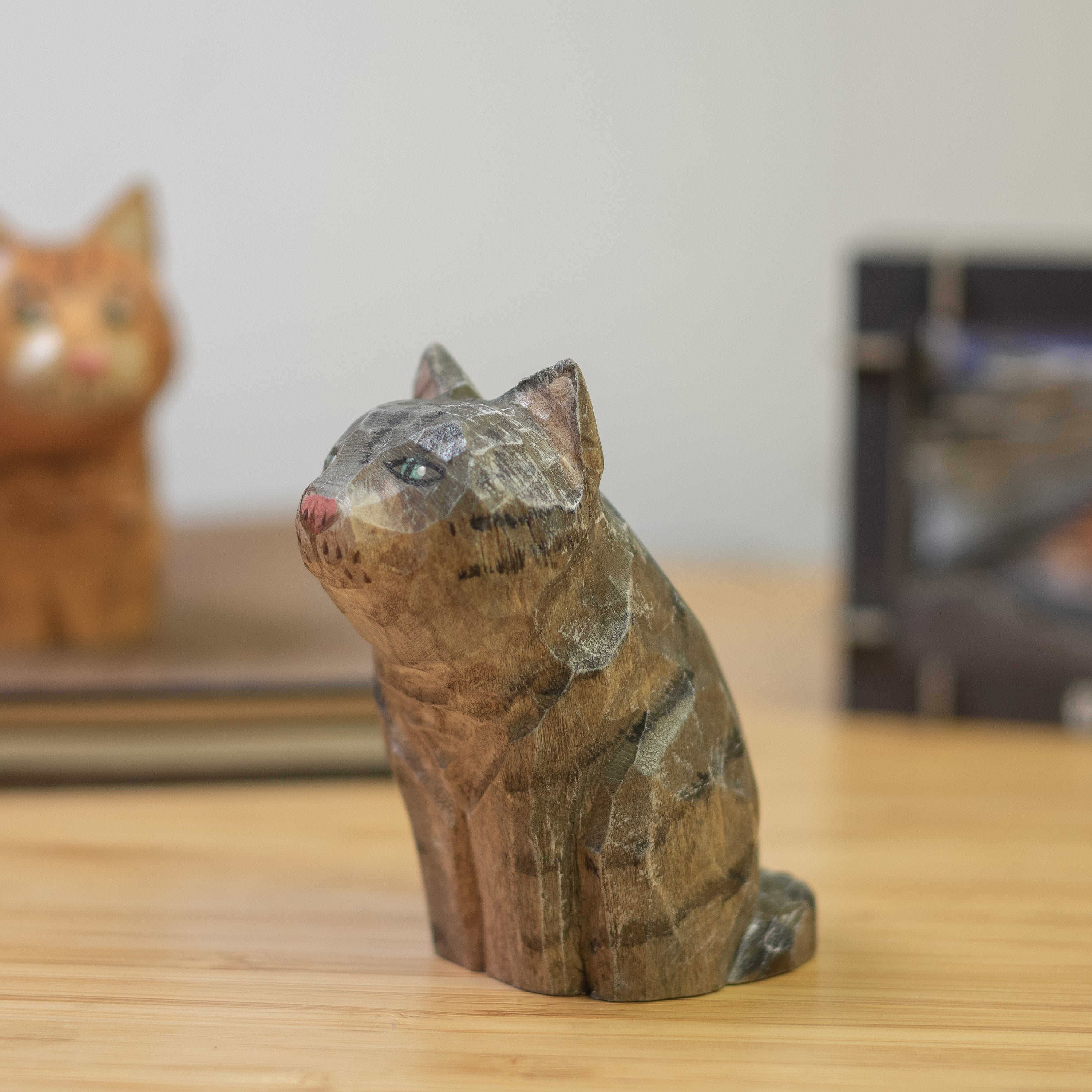 A hand-carved wooden figurine of a gray tabby cat, placed on a wooden surface.