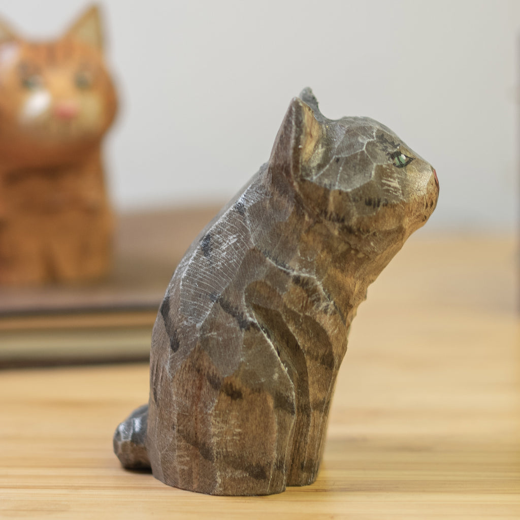 A hand-carved wooden figurine of a gray tabby cat, placed on a wooden surface.