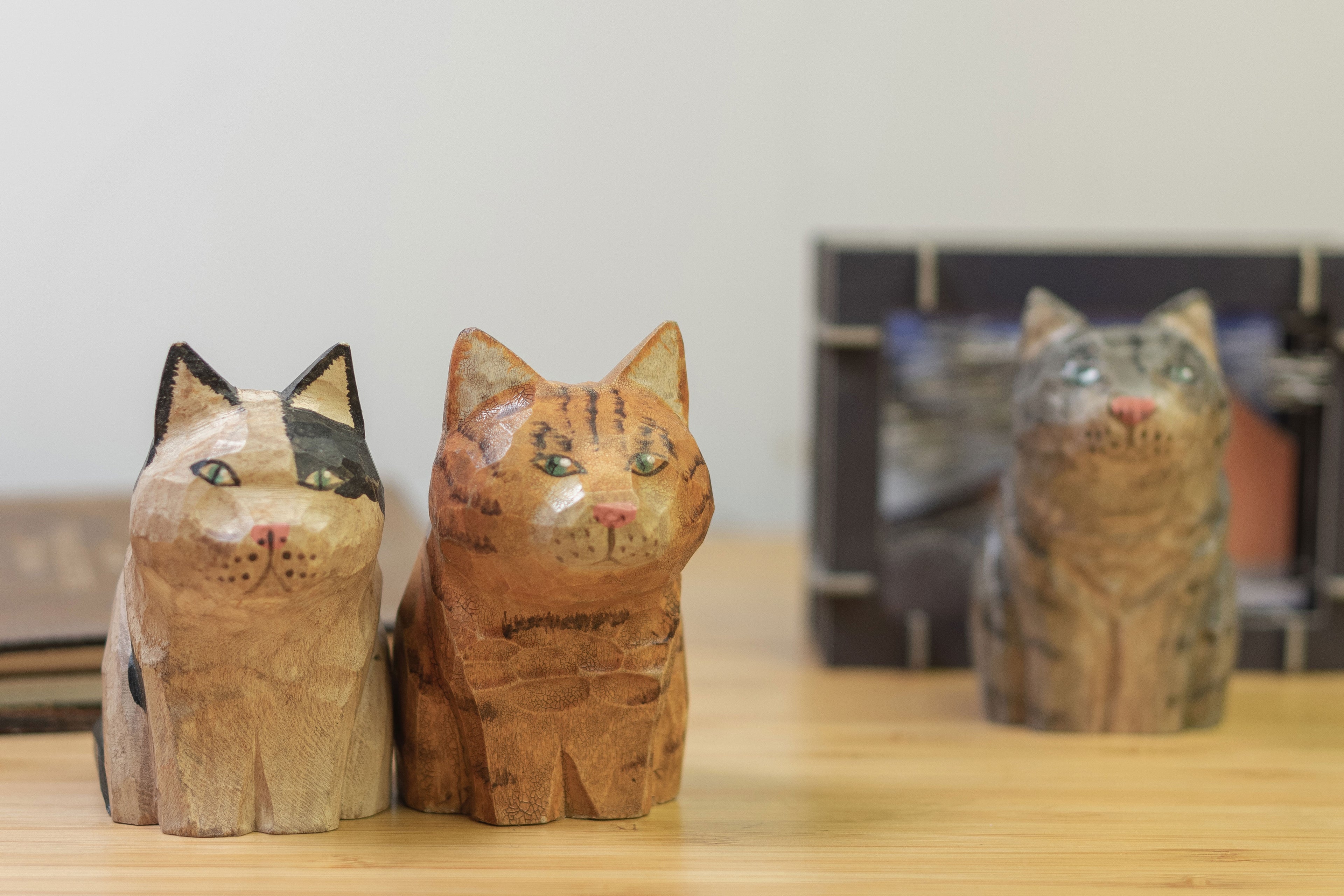 A series hand-carved wooden figurine of a gray tabby cat,  orange tabby and a calico cat