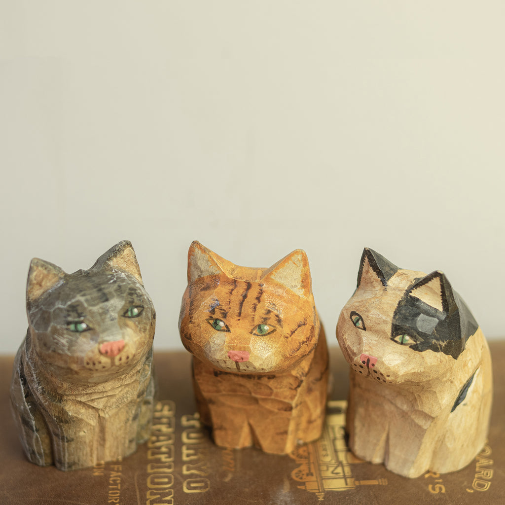 A series hand-carved wooden figurine of a gray tabby cat,  orange tabby and a calico cat