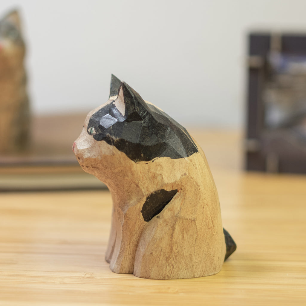 A hand-carved wooden figurine of a calico cat with a vintage finish, sitting  on a wooden surface.