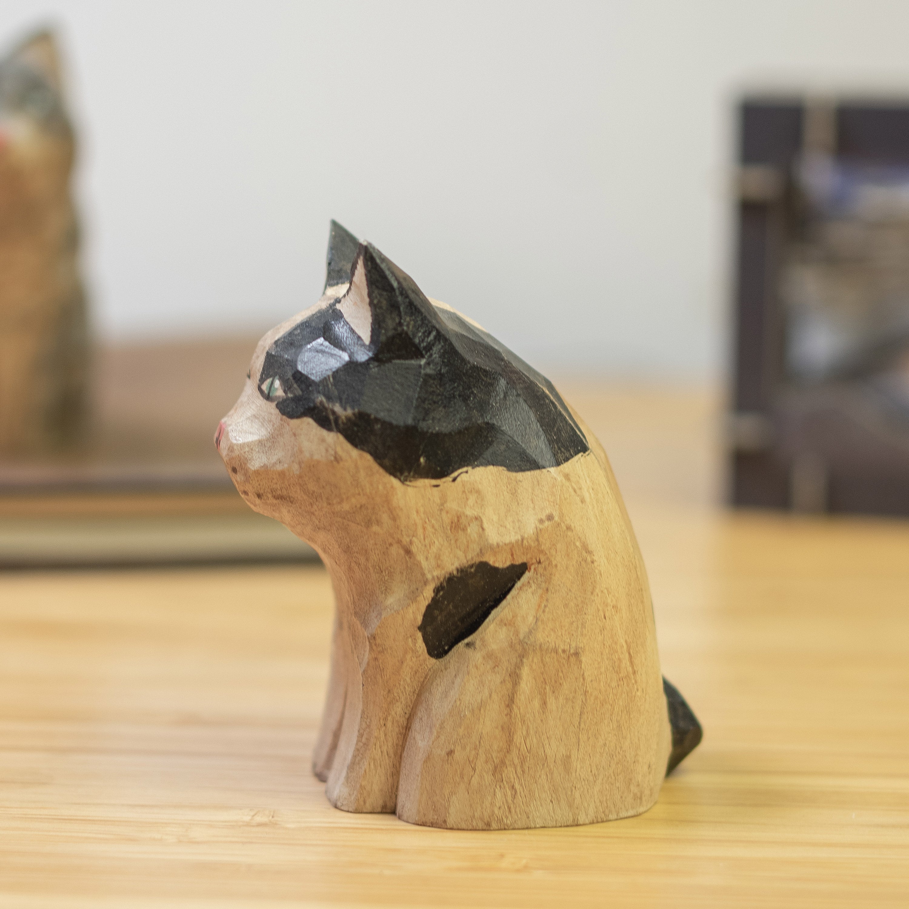 A hand-carved wooden figurine of a calico cat with a vintage finish, sitting  on a wooden surface.