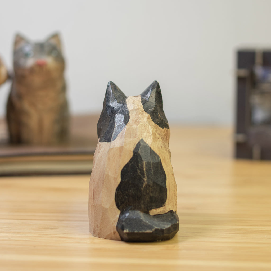 A hand-carved wooden figurine of a calico cat with a vintage finish, sitting  on a wooden surface.