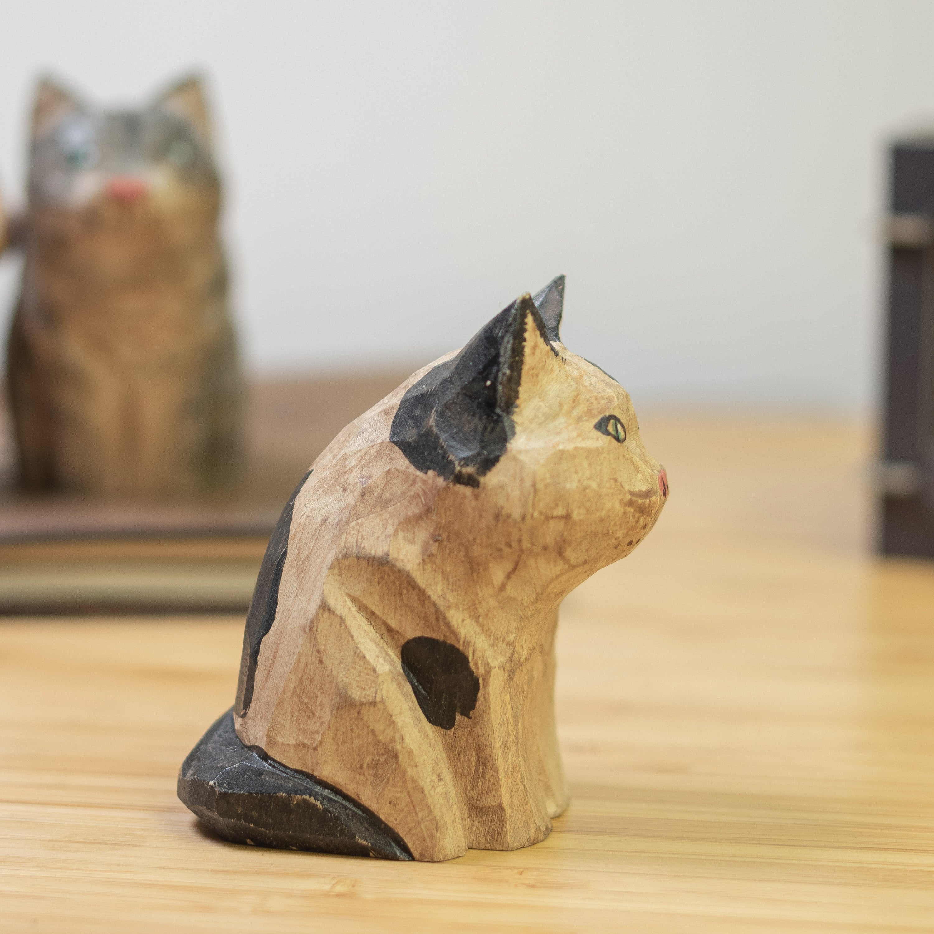 A hand-carved wooden figurine of a calico cat with a vintage finish, sitting  on a wooden surface.
