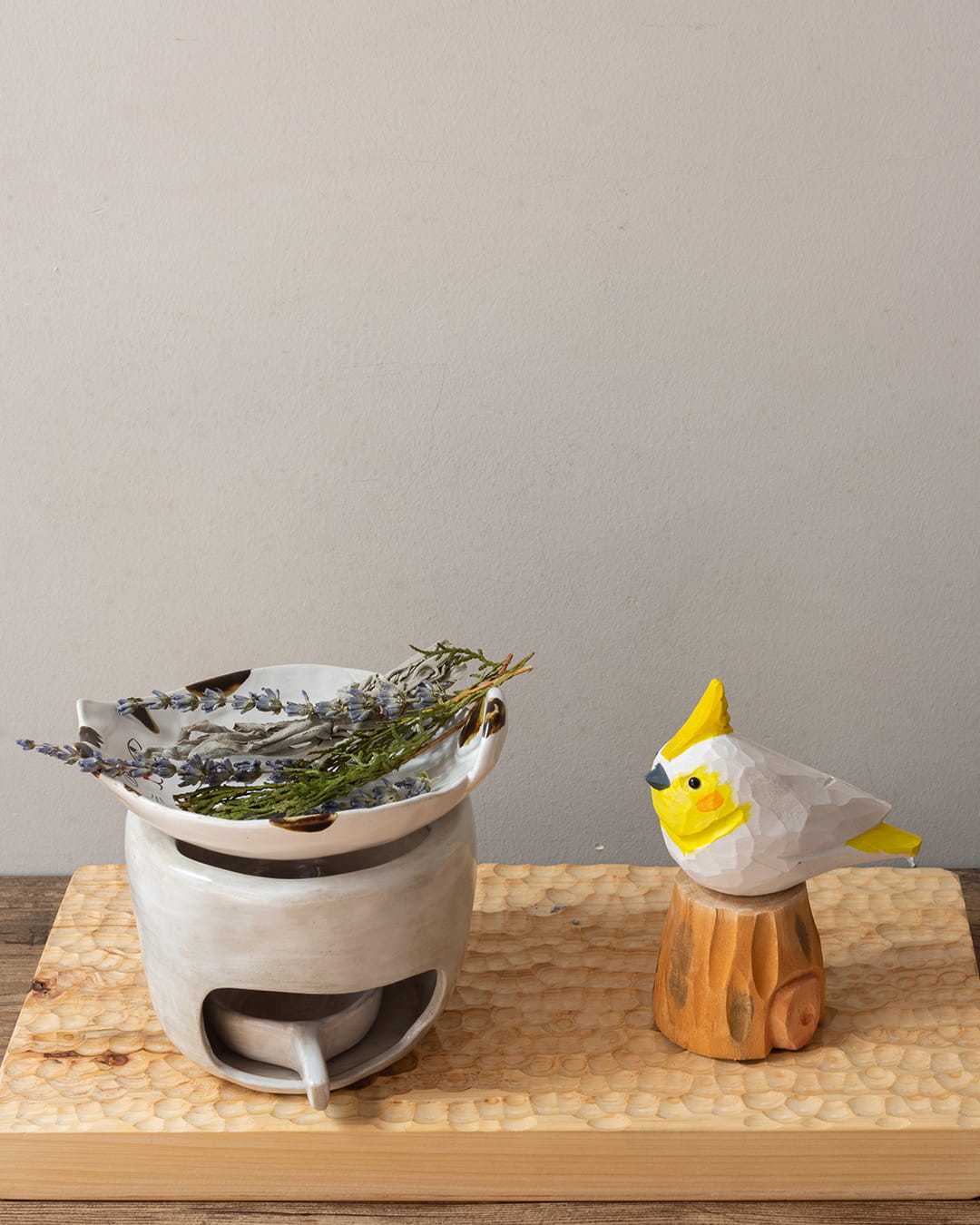 White ceramic incense burner with dried herbs on a wooden surface, next to a small wooden bird figurine.