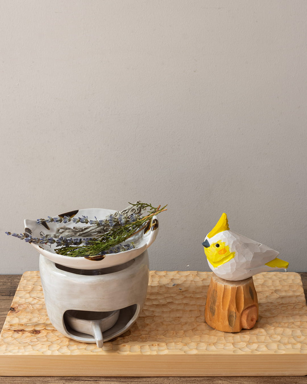 White ceramic incense burner with dried herbs on a wooden surface, next to a small wooden bird figurine.