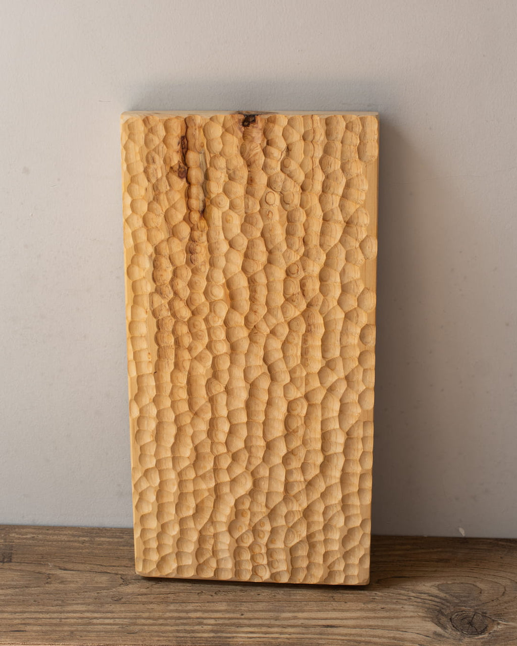 A rectangular, solid wood tray with a deep, hand-chiseled honeycomb texture, shown standing vertically on a dark wood surface.