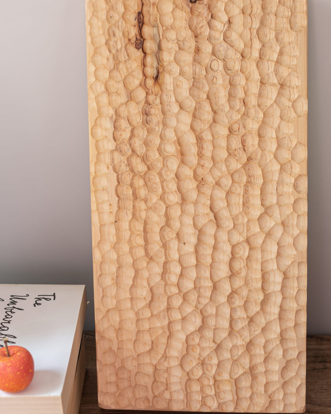 A rectangular, solid wood tray with a deep, hand-chiseled honeycomb texture, shown standing vertically on a dark wood surface.