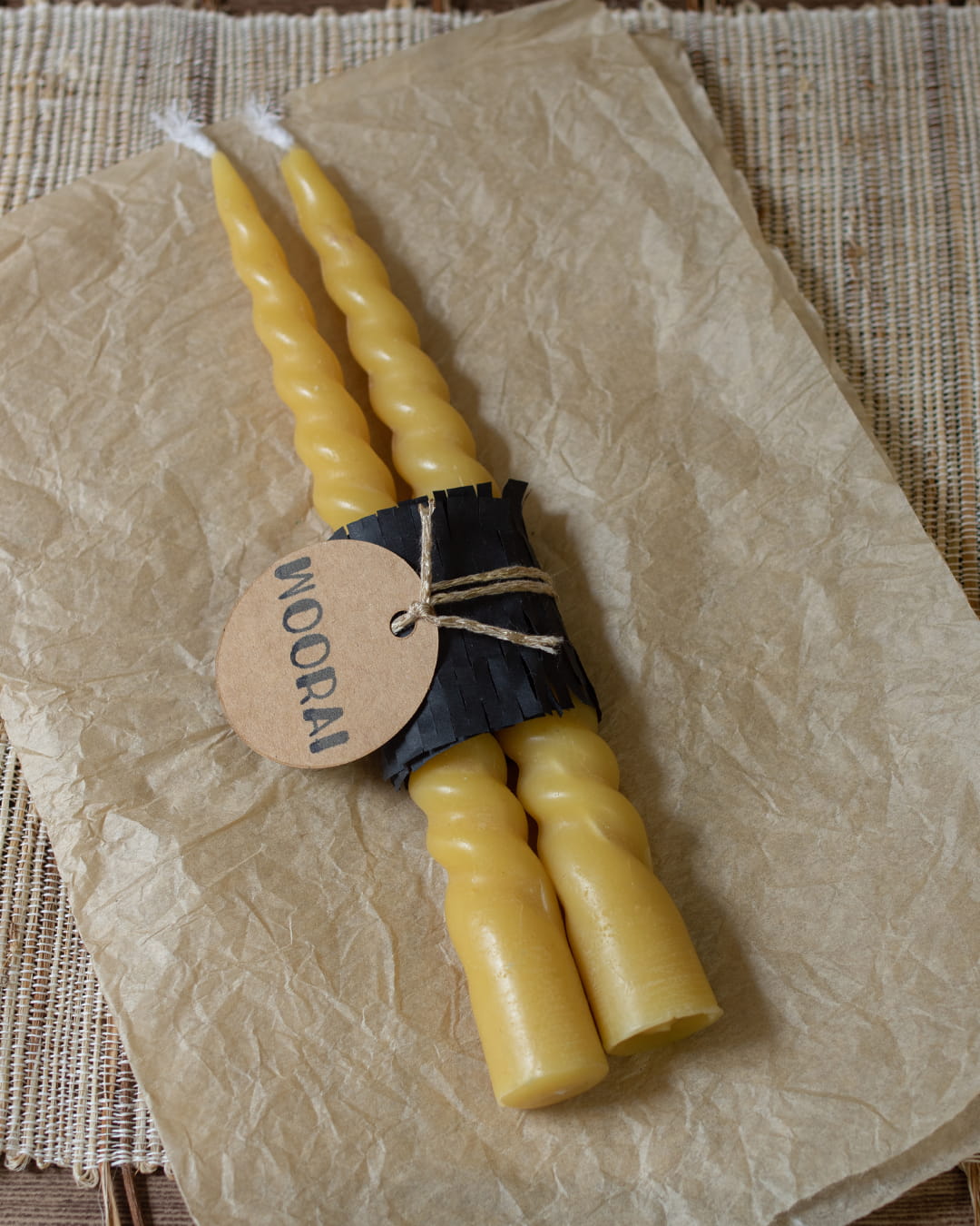 A pair of 8-inch spiral-twisted beeswax taper candles, bundled in black paper with a tag.