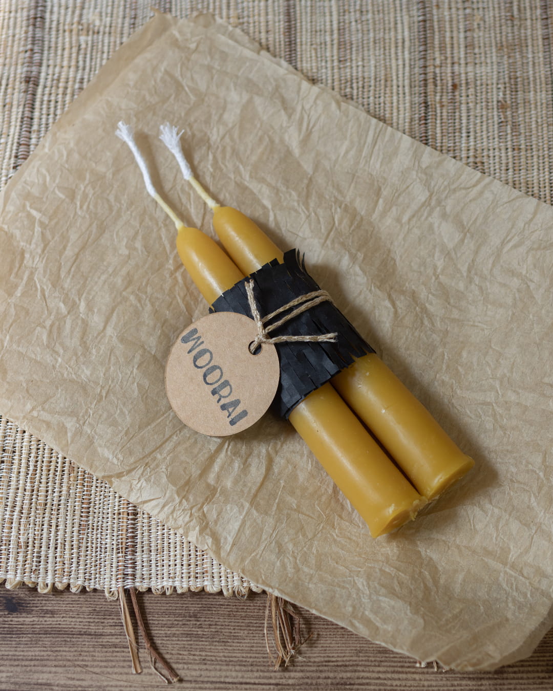 A pair of short, 5.5-inch smooth, hand-dipped beeswax taper candles, bundled in black paper with a tag.