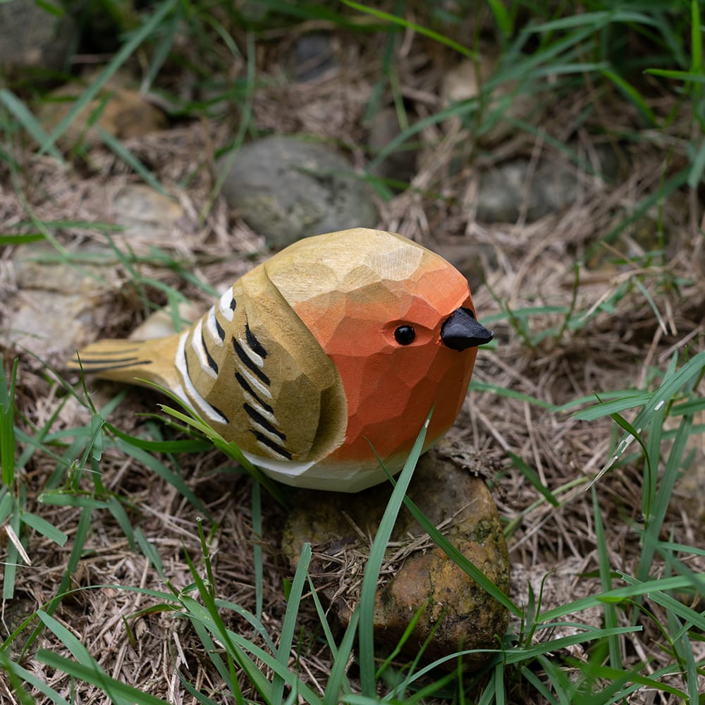 Wooden european robin figurine with colorful patterns on a grassy background