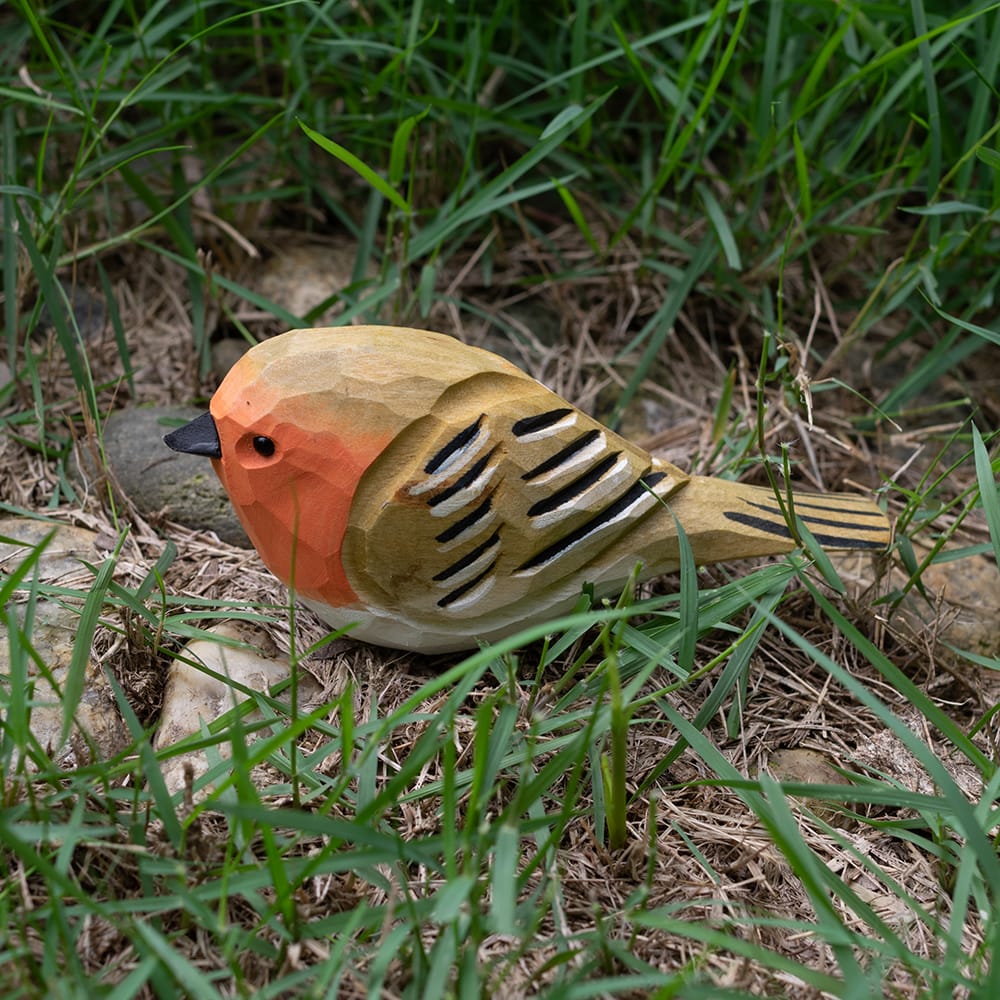 Wooden european robin figurine with colorful patterns on a grassy background