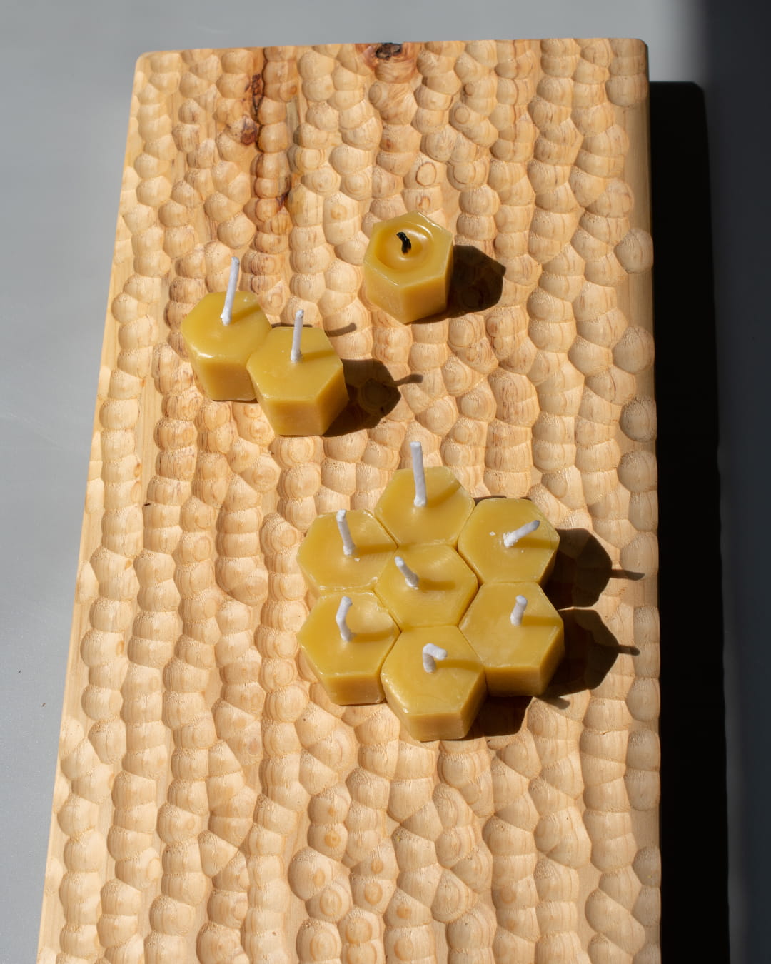 Several small, hexagonal honeycomb-shaped beeswax tealight candles, with one lit, on a wooden surface.