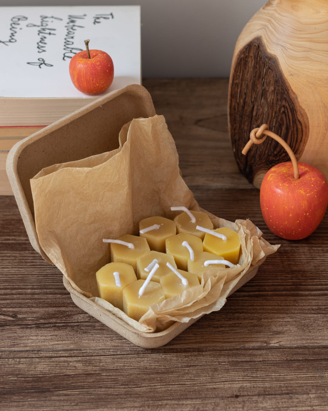 Several small, hexagonal honeycomb-shaped beeswax tealight candles, with one lit, on a wooden surface.