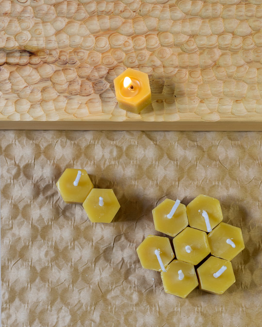 Several small, hexagonal honeycomb-shaped beeswax tealight candles, with one lit, on a wooden surface.
