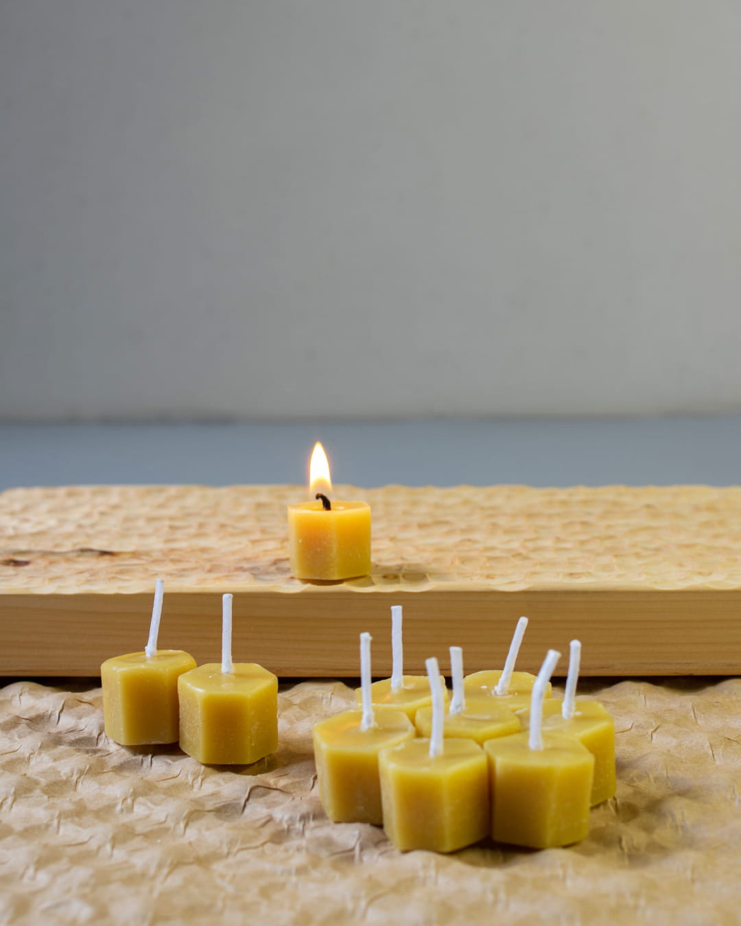 Several small, hexagonal honeycomb-shaped beeswax tealight candles, with one lit, on a wooden surface.