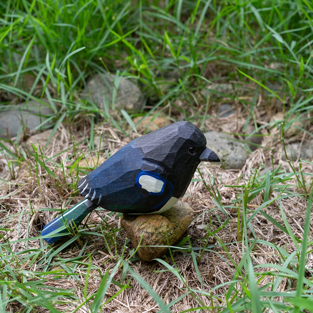 Wooden magpie figurine with black and blue plumage on a rock in a natural setting