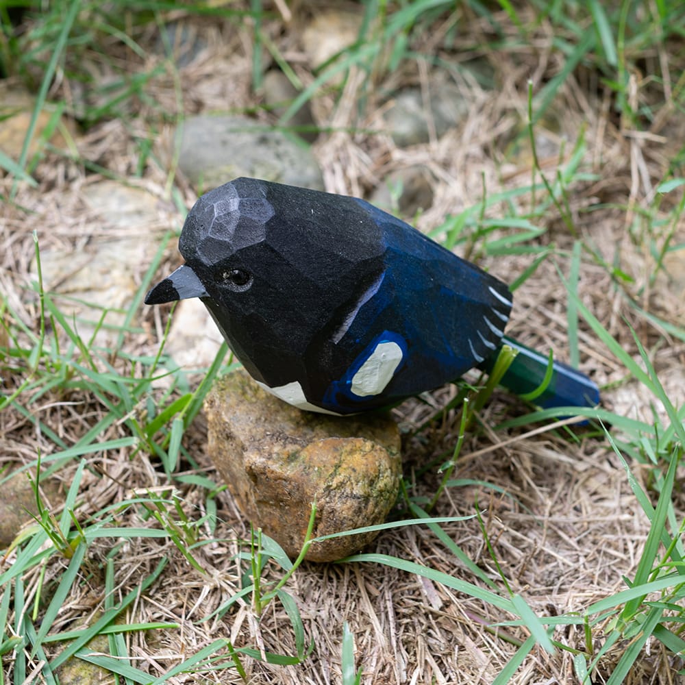Wooden magpie figurine with black and blue plumage on a rock in a natural setting
