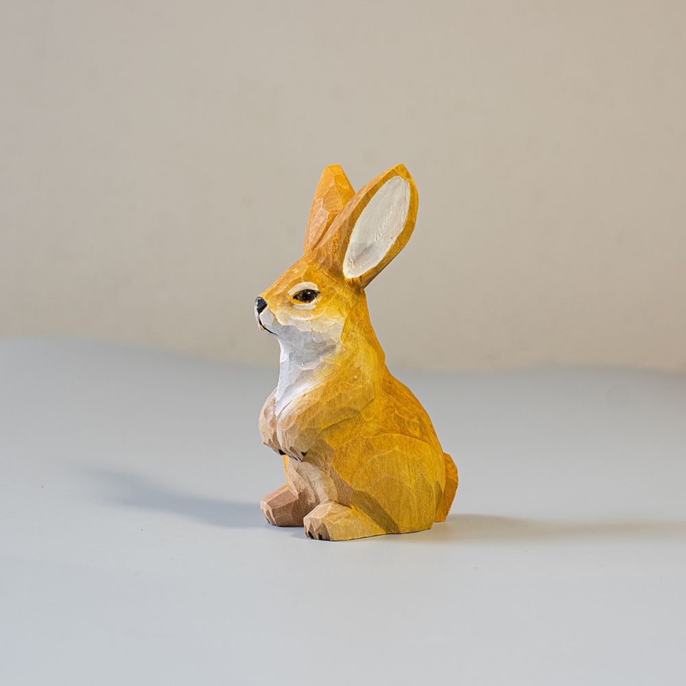 Wooden rabbit figurine on a light gray surface with a beige background