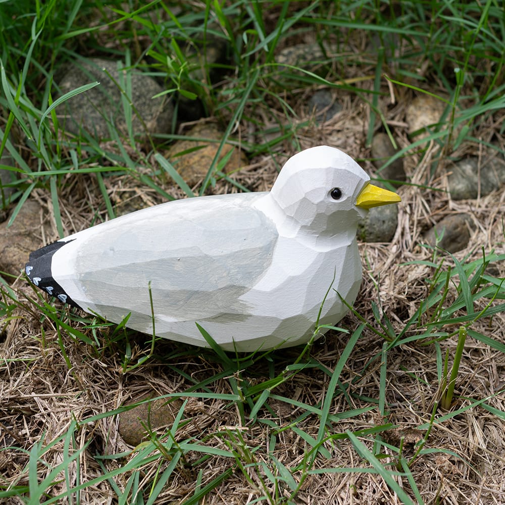 Wooden seagull figurine sitting on grass