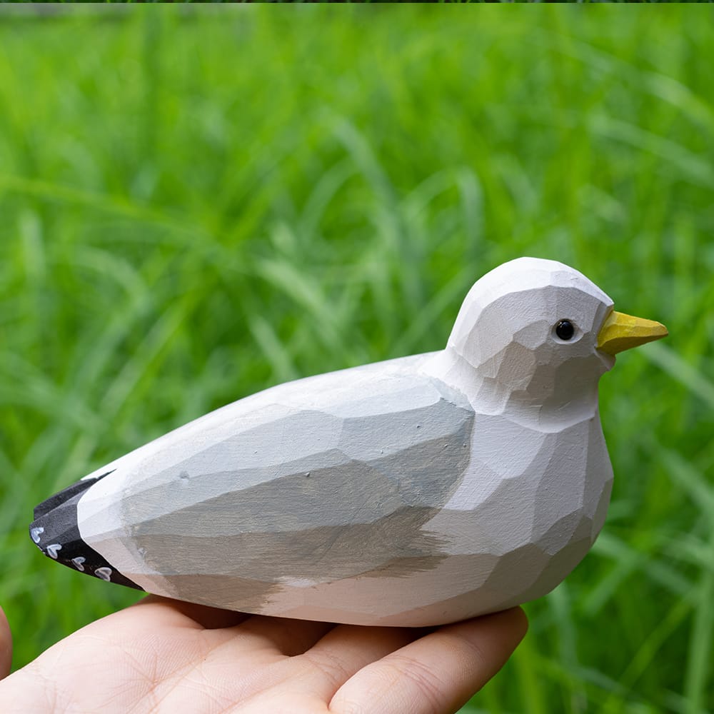 Wooden seagull figurine held in hand with green grass background