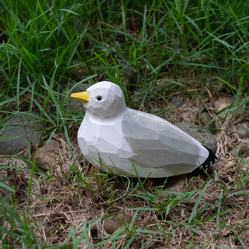 Wooden seagull figurine sitting on grass
