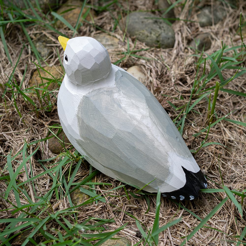 Wooden seagull figurine sitting on grass