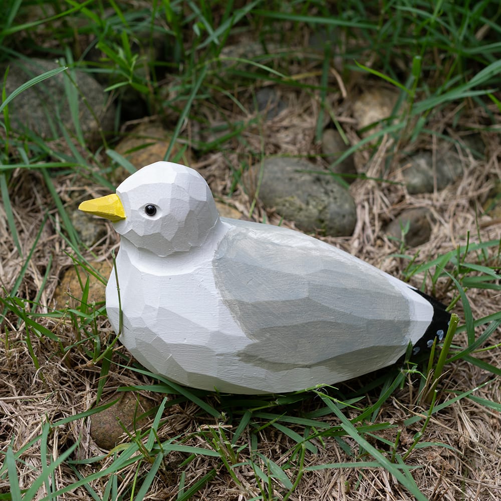 Wooden seagull figurine sitting on grass