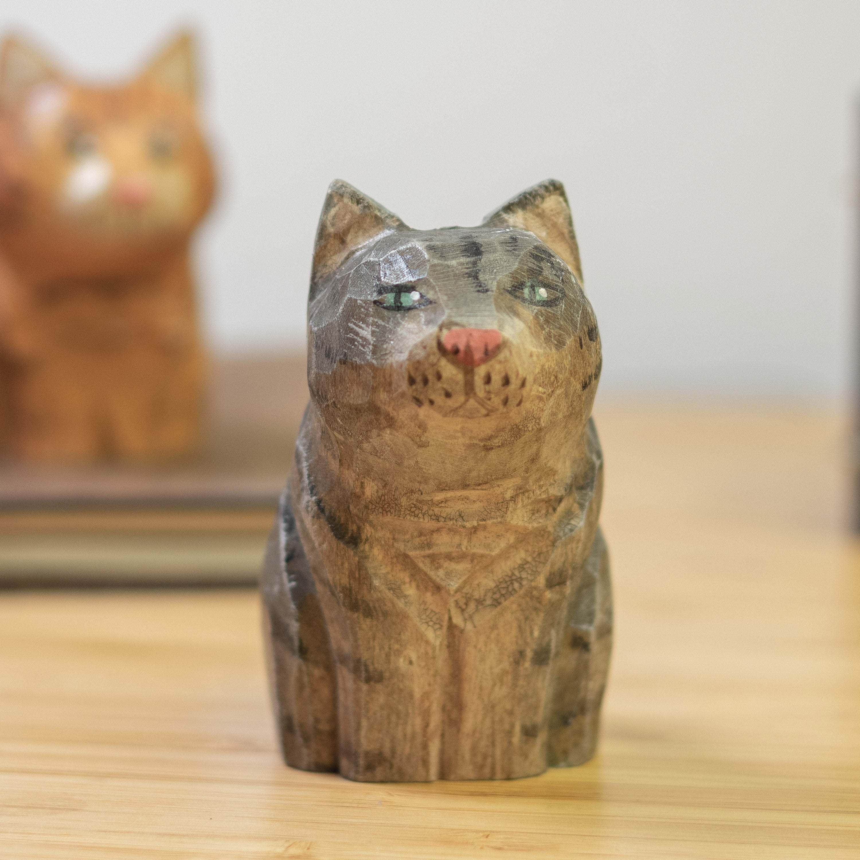 A hand-carved wooden figurine of a gray tabby cat, placed on a wooden surface.