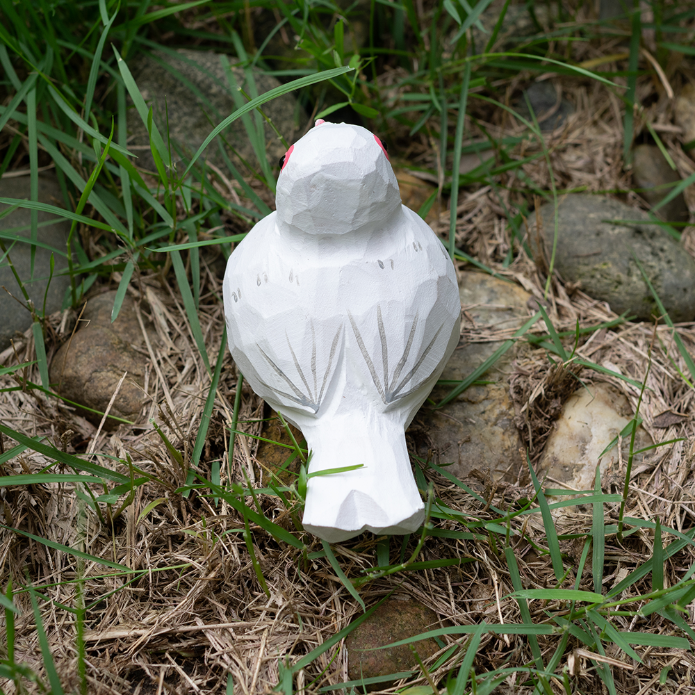 wooden white pigeon figurine sitting on grass and rock