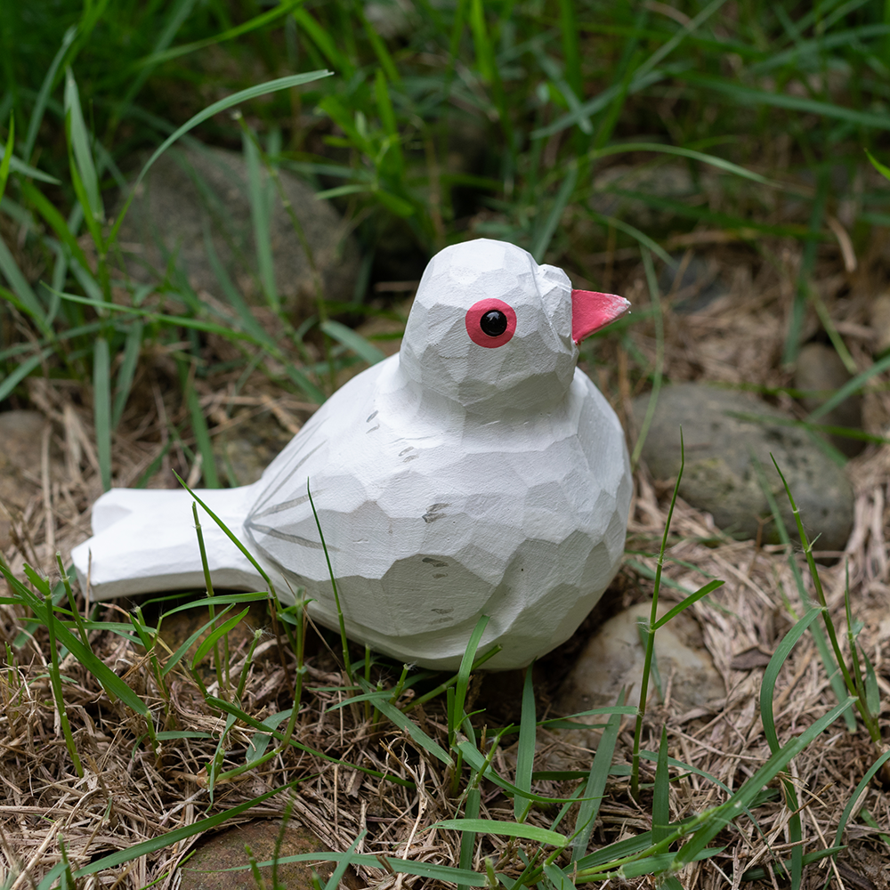 wooden white pigeon figurine sitting on grass and rock