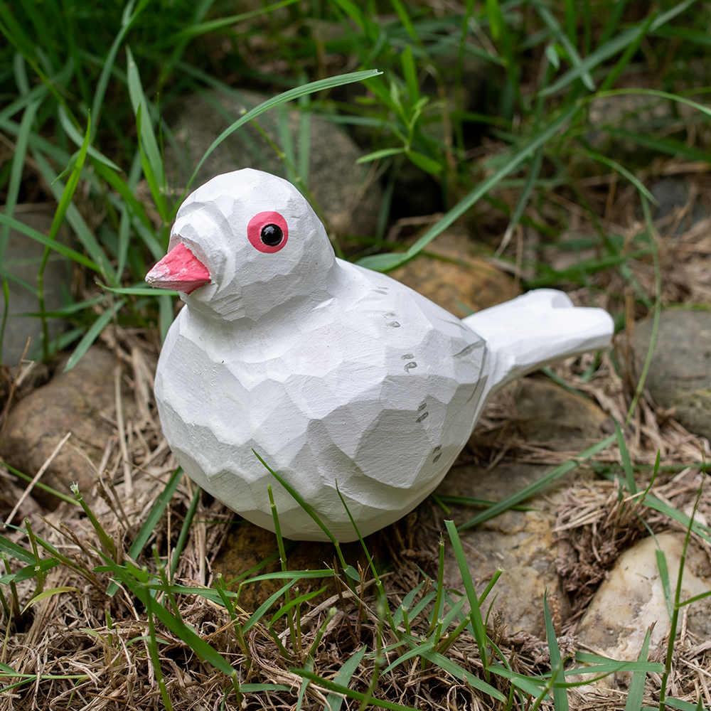 wooden white pigeon figurine sitting on grass and rock